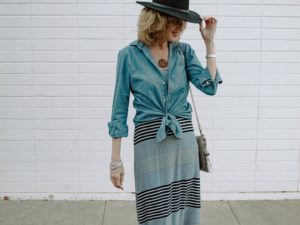 Woman wearing denim shirt over striped dress and black hat