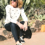 woman sitting at the Desert Botanical Gardens and wearing polka dot sweater, jeans, and adidas comfort sneakers