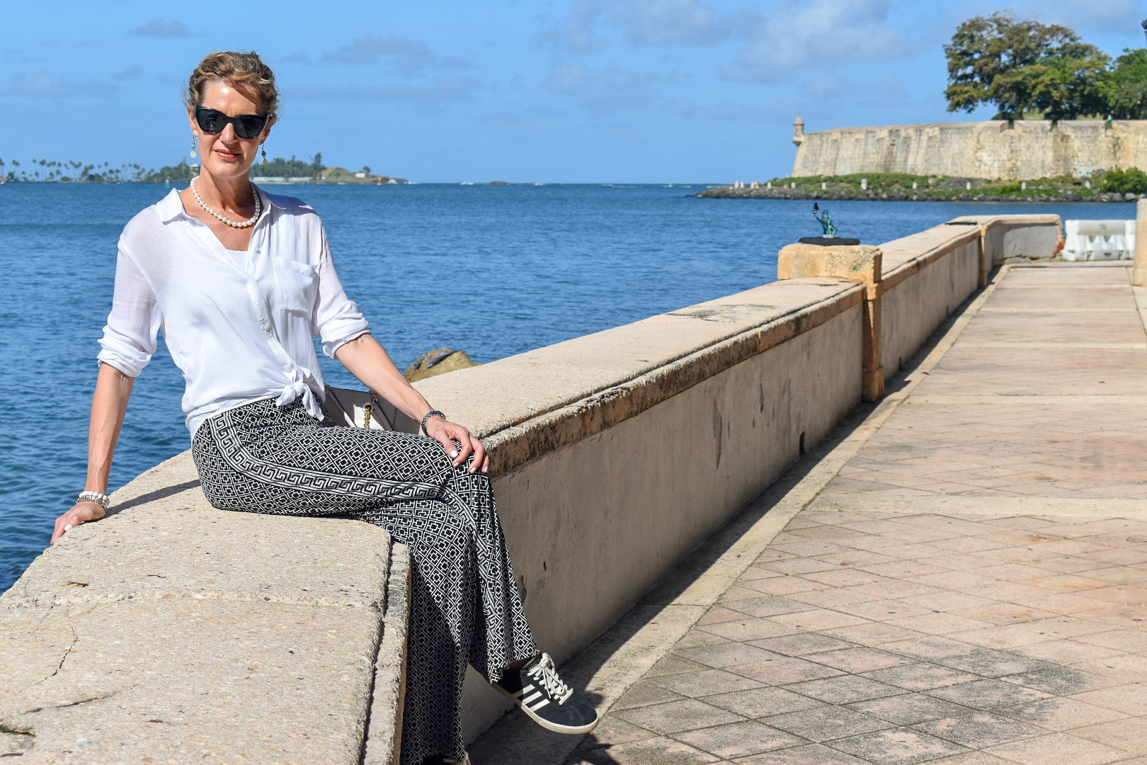 woman sitting on sea wall in old san juan puerto rico wearing palazzo pants and adidas sneakers-2